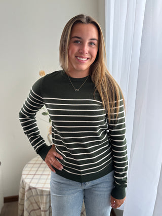 Woman wearing a black and white striped sweater in a room with a bed and curtains.