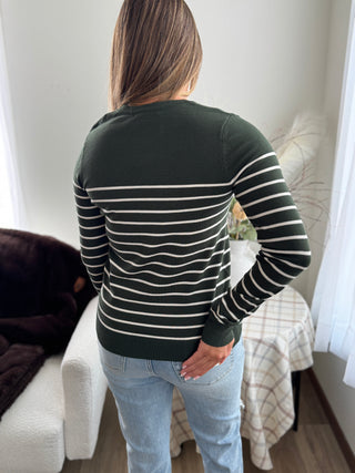 Person wearing a black and white striped sweater in a room with a bed and window.