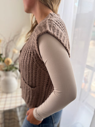 Person wearing a brown knitted vest with a blurred background