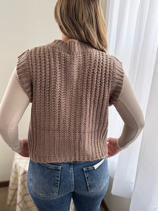 Person wearing a brown knitted vest with a neutral background