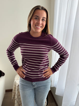 Woman wearing a purple striped sweater and light blue jeans indoors.