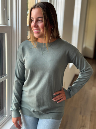 Woman wearing a green sweater standing indoors near a window.