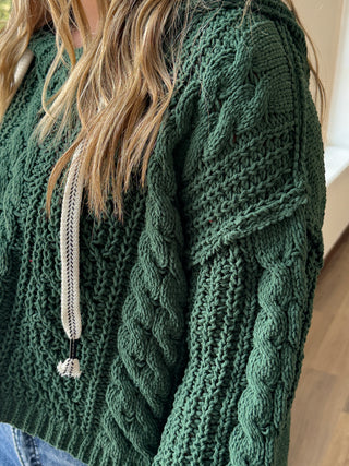 Green knitted sweater with cable pattern on a wooden surface