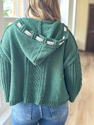Green knitted sweater with hood worn by a person indoors.