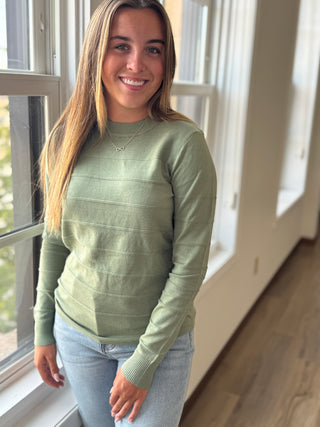 Woman wearing a green sweater standing indoors near a window