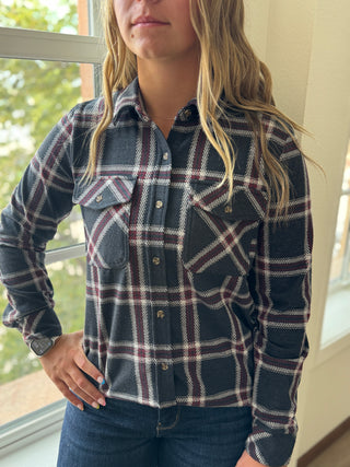 Person wearing a plaid shirt standing indoors near a window