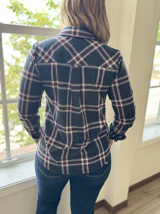 Person wearing a blue plaid jacket standing by a window