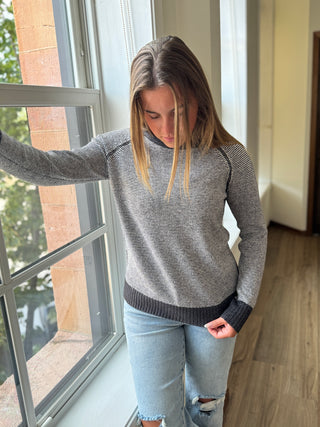 Woman wearing a plaid shirt and jeans standing against a stone wall.