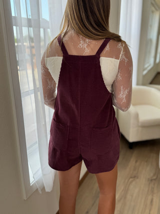 Person wearing a maroon romper with sheer sleeves in a well-lit room.