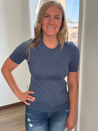 Woman wearing a blue shirt and jeans standing indoors.
