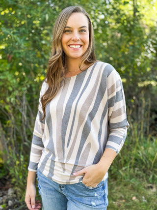 Woman in a gray and cream zebra stripe batwing knit sweater with jeans | V-Rae's Boutique