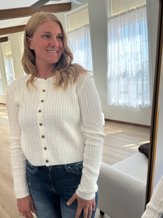 Woman wearing a white sweater and blue jeans sitting on a couch.