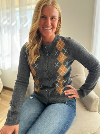 Woman wearing a gray sweater with argyle pattern sitting on a couch.