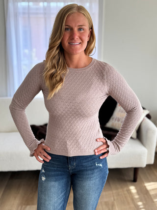 Woman wearing a beige sweater and blue jeans standing in a living room.