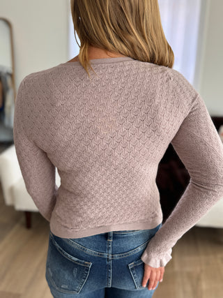 Person wearing a beige patterned sweater and blue jeans in an indoor setting