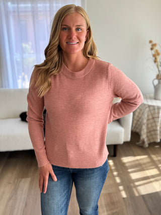 Woman wearing a pink sweater and blue jeans in a living room setting