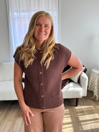 Woman wearing a brown knitted cardigan in a room with furniture and decor.