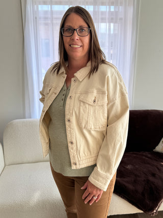 Person wearing a beige jacket in a room with a window and couch.