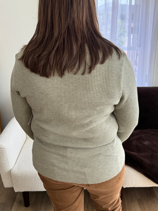 Person wearing a beige sweater and brown pants sitting on a white couch.