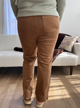 Person wearing brown pants sitting on a white couch with a neutral background