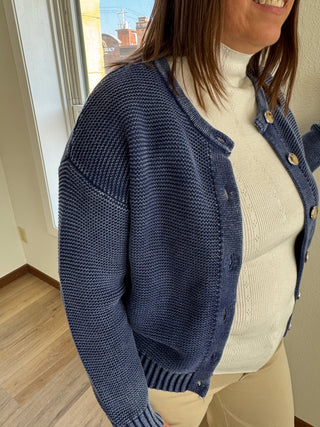 Person wearing a navy blue knitted cardigan over a white sweater.