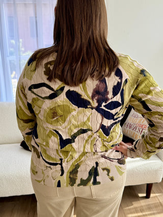 Person wearing a floral-patterned jacket in a room with a couch and window.