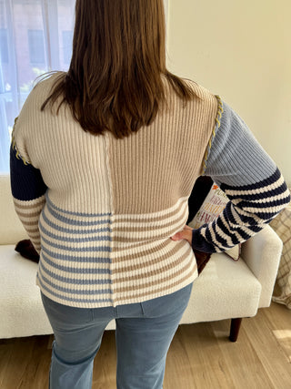 Person wearing a patterned sweater with a neutral vest over it in a living room setting.