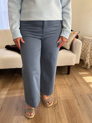 Person wearing gray pants and sandals sitting on a couch with a wooden floor.