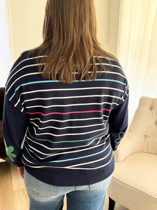 Person wearing a navy blue sweater with colorful stripes indoors.