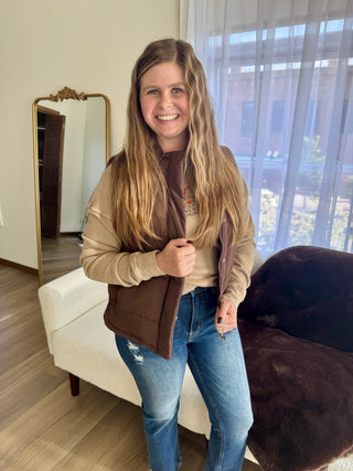 Woman wearing a brown vest over a beige sweater in a living room.