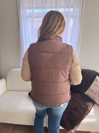 Person wearing a brown puffer jacket sitting on a couch with a window in the background