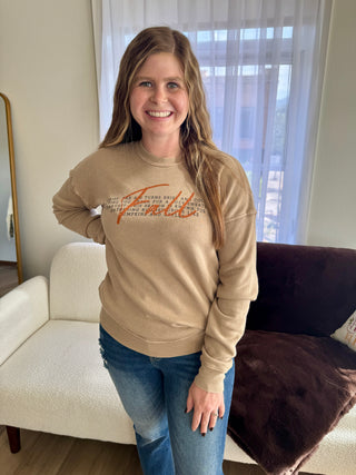 Woman wearing a beige sweatshirt with text, standing in a living room.