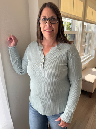 Woman wearing a light gray sweater and glasses indoors.