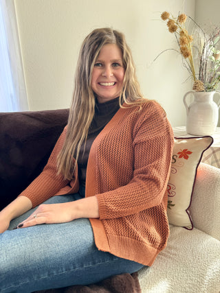 Woman sitting on a couch wearing a brown cardigan in a cozy living room.