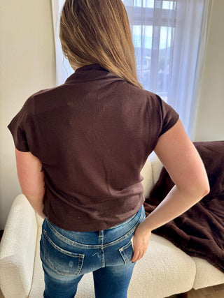 Person wearing a brown shirt and blue jeans standing in a room with a window in the background.