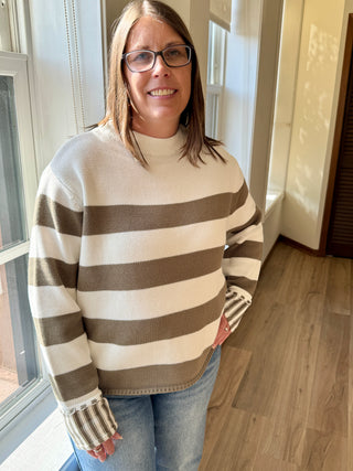 Woman wearing a striped sweater standing indoors near a window.