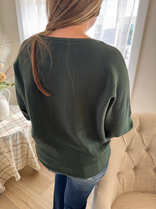 Person wearing a green beanie in a room with a window and chair.