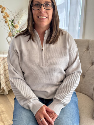 Woman wearing a beige long-sleeve shirt sitting on a couch in a living room.