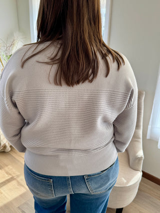 Person wearing a light gray sweater and blue jeans in an indoor setting