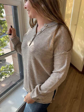 Person wearing a textured sweater standing indoors with a window in the background