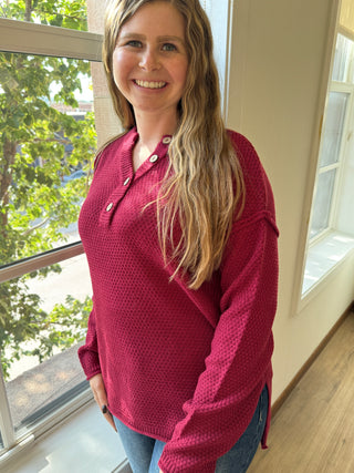 Woman wearing a red sweater standing indoors with a window in the background