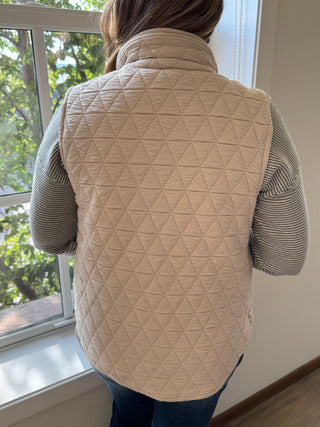 Person wearing a beige quilted jacket with a window in the background
