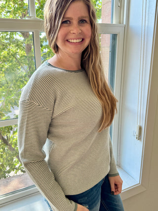 Woman wearing a striped sweater standing by a window with greenery outside