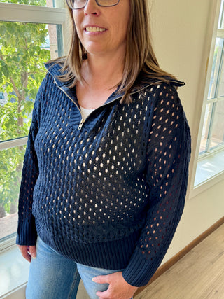 Woman wearing a navy blue perforated sweater standing indoors near a window.