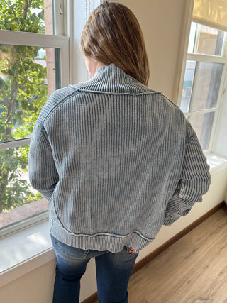 Person wearing a gray jacket standing indoors near a window