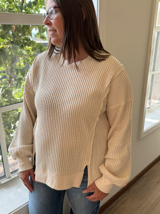 Person wearing a beige sweater in a room with large windows