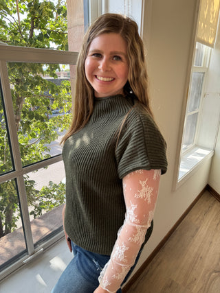 Woman wearing a green sweater with lace sleeves indoors