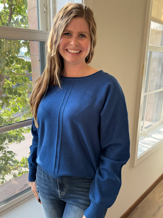 Person wearing a blue sweater standing indoors with a window in the background