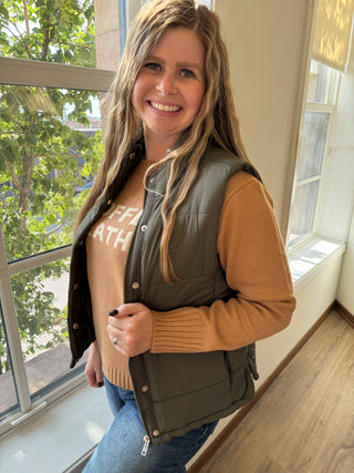 Woman wearing a brown jacket with a visible brand logo, standing indoors.