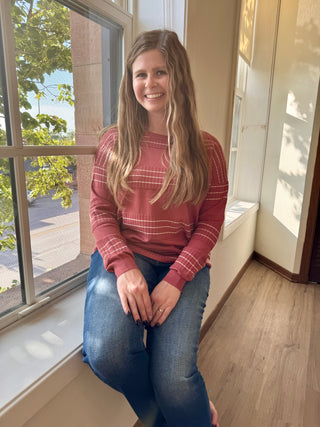 Woman sitting on a windowsill wearing a red plaid shirt and blue jeans, smiling.